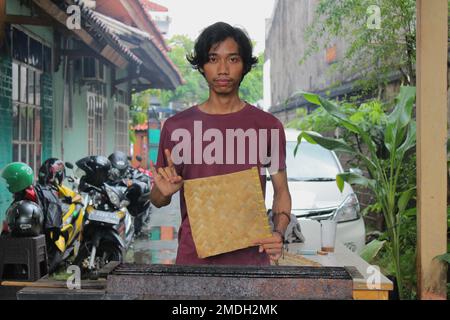 Giacarta, Indonesia - 02 24 2020: Un uomo che tiene un ventilatore e che mostra un dito di metallo con una faccia piatta mentre brucia il cibo durante una vacanza all'università nella Jaka Foto Stock