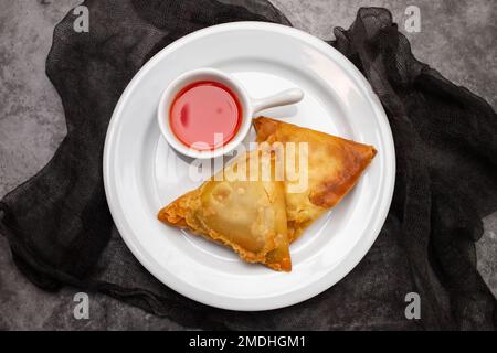 Due samosa con carne e verdure su un piccolo piatto bianco Foto Stock