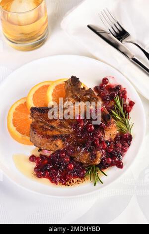 Braciole di maiale fritte servite con salsa ai mirtilli con arancia e rosmarino. Sono eleganti per un pranzo o una cena. Foto Stock