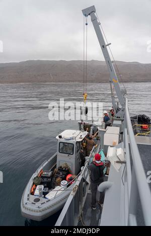 I marinai assegnati all'unità mobile di smaltimento delle ordigni esplosive (EODMU) 11 a bordo di un'imbarcazione gonfiabile a scafo rigido (RHIB) assistono i contraenti civili ad azionare una gru a bordo di Research Craft (RCS) 1 per sollevare un motore fuoribordo a bordo di RC 1 durante un esercizio di addestramento antincendio in diretta al largo della costa di San Clemente Island, 24 agosto 2022. Il live Fire di MCM è una formazione realistica e pertinente che consente alle nostre forze comuni e multidominio di integrare e provare una capacità critica e competenze complesse. Foto Stock