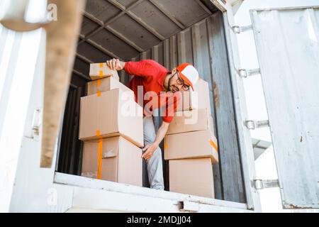 l'addetto alla consegna in rosso scarica diverse scatole da un contenitore Foto Stock