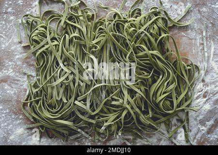Pasta fresca. Fettuccine crude italiane fatte in casa con spinaci su sfondo di tavola in legno. Foto di alta qualità Foto Stock
