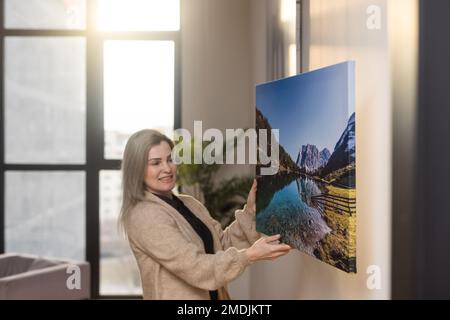 Stampa canvas con wrap galleria. Donna appende la fotografia su una parete bianca. Stampa di tela fotografica con le mani in mano Foto Stock