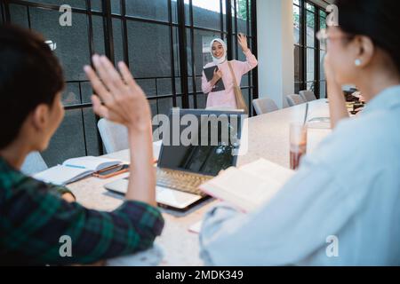 Allievo asiatico in hijab ondeggiando mentre incontra il suo amico Foto Stock