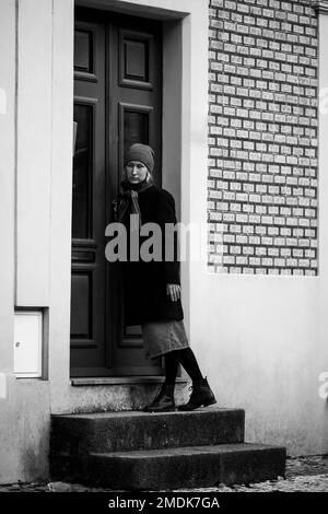 Una donna triste sul portico della casa bussa alla porta. Foto in bianco e nero. Foto Stock