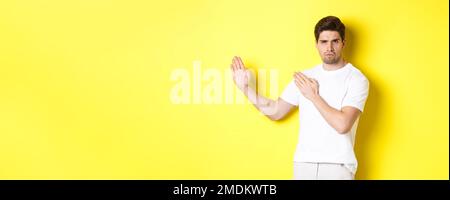 Uomo che mostra abilità kung-fu, arti marziali movimento ninja, in piedi in bianco t-shirt pronto a combattere, in piedi su sfondo giallo Foto Stock