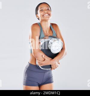 Dieta, perdita di peso e scala con un atleta nero donna in studio su uno sfondo grigio per la positività del corpo o la salute. Fitness, peso e perdere Foto Stock