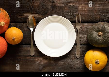 piatto bianco sul tavolo e accanto a zucche su un vecchio tavolo di legno, decorazione impostazione tavolo festivo, piatto sul tavolo Foto Stock