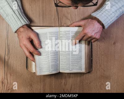 Caen, Francia 2023. Uomo che legge un vecchio libro vista dall'alto, tavolo di legno Foto Stock