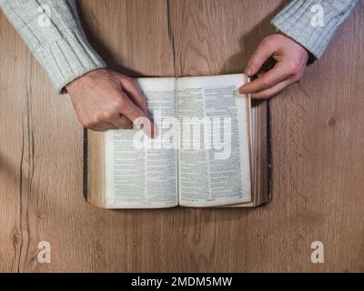 Caen, Francia 2023. Uomo che legge un vecchio libro vista dall'alto, tavolo di legno Foto Stock