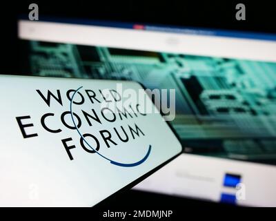 Smartphone con logo dell'organizzazione World Economic Forum (WEF) sullo schermo di fronte al sito Web. Messa a fuoco al centro a sinistra del display del telefono. Foto Stock