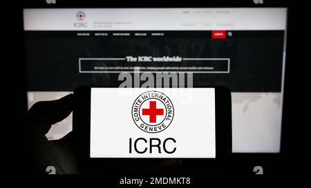 Persona che tiene il cellulare con il logo del Comitato Internazionale della Croce Rossa (CICR) sullo schermo di fronte alla pagina web. Messa a fuoco sul display del telefono. Foto Stock