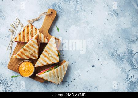 Quattro panini fatti in casa con salsiccia, formaggio e rucola su un fondo di cemento chiaro Foto Stock