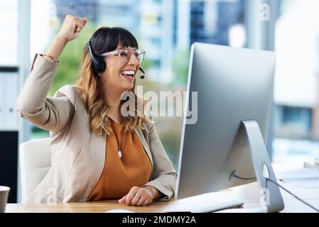 Congratulazioni. una giovane e attraente donna d'affari che festeggia mentre indossa una cuffia nel suo ufficio durante il giorno. Foto Stock