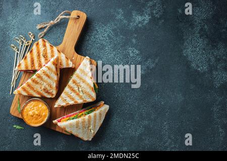 Quattro panini fatti in casa con salsiccia, formaggio e rucola su fondo di cemento scuro Foto Stock