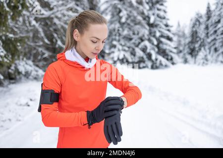 Una runner femminile controlla le sue prestazioni sportive utilizzando un orologio intelligente. Correre in inverno e misurare la frequenza cardiaca. Foto Stock