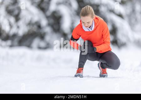 Una giovane donna in forma tiene un ginocchio rinforzato dopo aver tendere il suo legamento crociato durante l'allenamento di fondo sulla neve durante la stagione invernale. Foto Stock