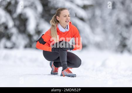 Una giovane donna in forma tiene un ginocchio rinforzato dopo aver tendere il suo legamento crociato durante l'allenamento di fondo sulla neve durante la stagione invernale. Foto Stock