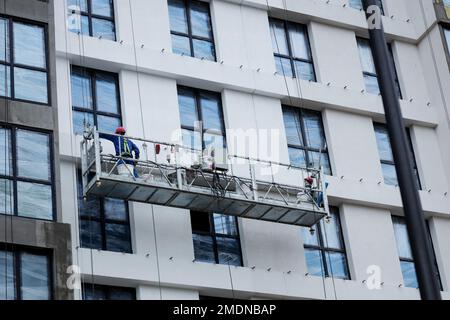 Un operatore in una culla di un meccanismo di sollevamento. Processo di isolamento delle pareti esterne in un edificio a più piani in costruzione. Foto Stock