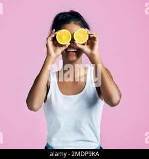 Una visione sana delle cose. Studio shot di una bella giovane donna in posa con arance sopra gli occhi su uno sfondo rosa. Foto Stock