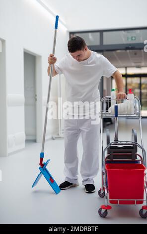 Giovane uomo con sindrome di Down che lavora in un ospedale come più pulito. Concetto di integrazione di persone con disabilità nella società. Foto Stock