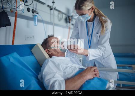 Giovane donna medico mettere su maschera di ossigeno per pazienti anziani. Foto Stock