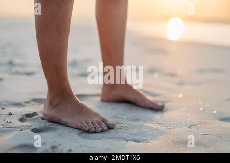 Primo piano dei piedi delle donne nella sabbia, in mare. Foto Stock