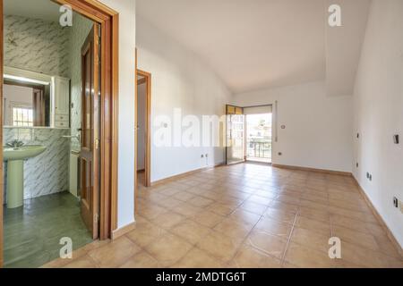 Grande camera vuota di una casa con pavimento in gres con bagno proprio e terrazza con porta in alluminio anodizzato marrone con gla arancione traslucido Foto Stock