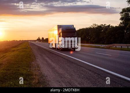 Un camion bianco con semirimorchio trasporta il carico sull'autostrada la sera sullo sfondo del tramonto. Rispetto delle norme del carr Foto Stock