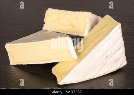 Tre pezzi di formaggio Brie fragrante su pietra ardesia, macro. Foto Stock