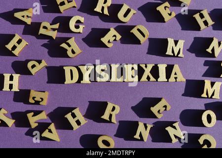 Dislessia, parola in lettere alfabetiche di legno circondata da lettere casuali su sfondo viola Foto Stock