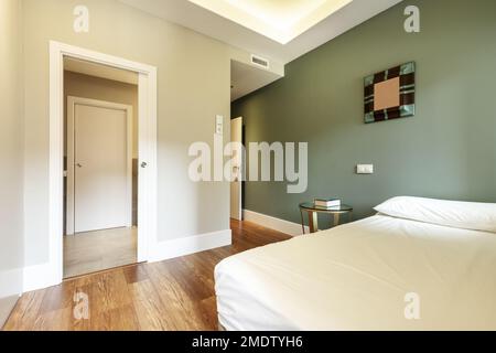 Una camera con un letto matrimoniale senza vestiti accanto ad una parete verde liscia e le opposte dipinte in grigio chiaro Foto Stock