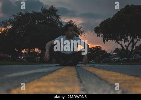 Un giovane ispanico seduto sulla strada Foto Stock