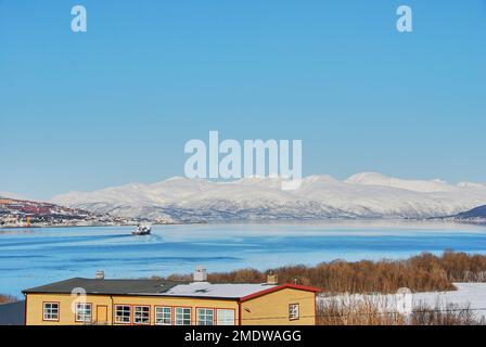 Peschereccio nel paesaggio invernale del porto di Tromso in un fiordo sulla costa settentrionale della Norvegia con montagne innevate nel backgroun Foto Stock