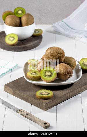 Kiwi fresco e fette su piatto bianco su base di legno bianco. Formato verticale. Foto Stock