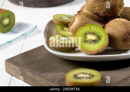 Chiudete il kiwi fresco e fettete su un piatto bianco su fondo di legno bianco. Messa a fuoco selettiva. Foto Stock