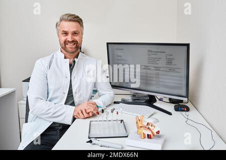 Audioprotetista seduto nel suo ufficio di reparto di audiologia durante la selezione di apparecchi acustici per il paziente. Apparecchi acustici e soluzioni Foto Stock