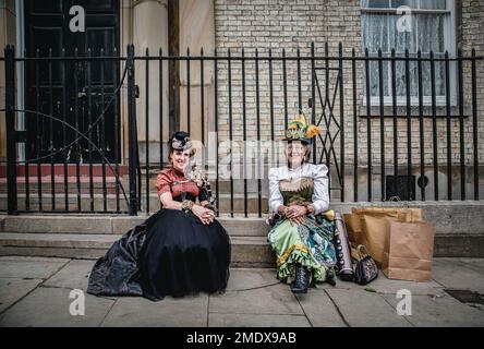 Due punk a vapore femminili vestiti in stile vittoriano seduti su un gradino della strada. Stewampunk femminile con costume d'epoca. Foto Stock