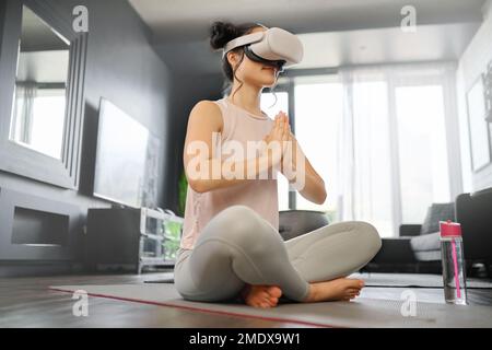 VR, meditazione e fitness con una donna che utilizza un visore per accedere al metaverse di casa sua per la salute. Realtà virtuale, yoga e esercizio fisico con a. Foto Stock