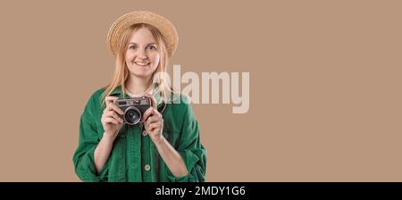 Bella donna ridente in cappello estivo e giacca verde tenendo in mano la macchina fotografica vintage e posa sullo sfondo in studio. Foto Stock