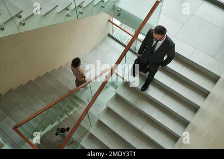 Vista dall'alto dei lavoratori di colletti bianchi multiculturali in formalwear che si spostano al piano inferiore all'interno di un moderno business center mentre si lascia dopo il lavoro Foto Stock