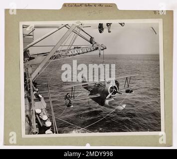 Una Guardia Costiera 'anatra' porta al mare. Coast Guardsman lancia un aereo di ricognizione dal ponte della loro taglierina da qualche parte nel Pacifico. In pochi secondi mani esperte uomo la gru che solleva l'aereo dalla sua culla e lo abbassa di lato. Due guardiani costieri cavalcano le ali nel processo di lancio per mantenere la nave in equilibrio. Una volta in mare, le linee sono gettate via e il 'Duck' come gli uomini d'equipaggio lo chiamano rasente la superficie e vola via. Foto Stock