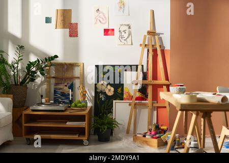 Parte dello studio di persona creativa con una varietà di articoli e attrezzature per il lavoro, schizzi su muro e piccolo lettore di dischi Foto Stock