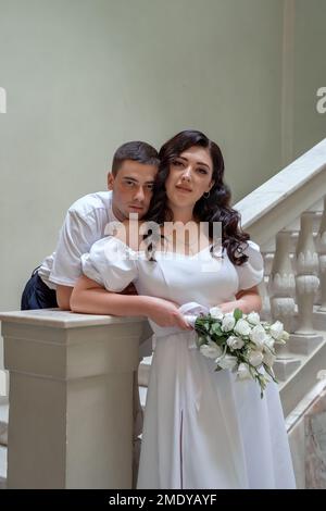 Vista frontale di eleganti sposi novelli, sposi in abiti da sposa lunghi e aderenti che reggono il bouquet Foto Stock