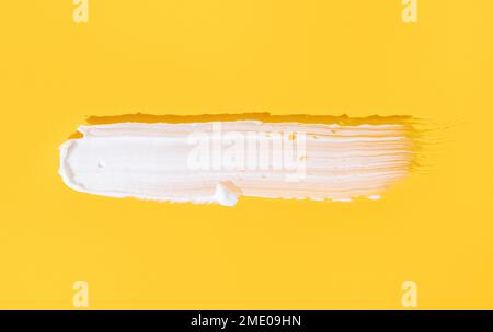 Striscio di crema cosmetica bianca isolato su sfondo giallo. Prodotto per la cura della pelle Foto Stock