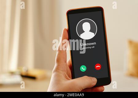 Mano femminile che tiene in mano uno smartphone mobile che visualizza una chiamata in arrivo da un chiamante sconosciuto. Concetto di chiamata spam sospetta telefonica. Foto Stock