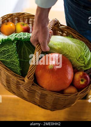 Vista in un cesto di vimini intrecciato tenuto da mano maschile, riempito con diversi tipi di verdure e frutta Foto Stock