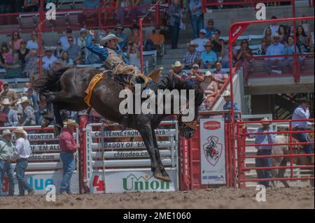 Un cowboy cavalca un bronco durante i Cheyenne Frontier Days, 26 luglio 2022, presso il Cheyenne Rodeo Grounds. Forte D.A. Russell e F.E Warren Air Force base hanno sostenuto Cheyenne Frontier Days fin dalla sua nascita nel 1897. Foto Stock