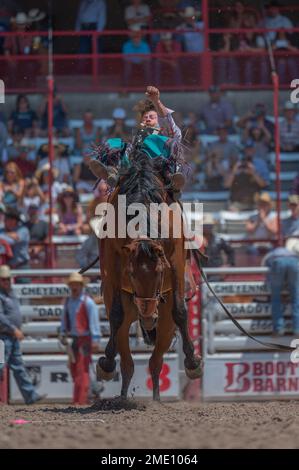 Un cowboy cavalca un bronco durante i Cheyenne Frontier Days, 26 luglio 2022, presso il Cheyenne Rodeo Grounds. Forte D.A. Russell e F.E Warren Air Force base hanno sostenuto Cheyenne Frontier Days fin dalla sua nascita nel 1897. Foto Stock