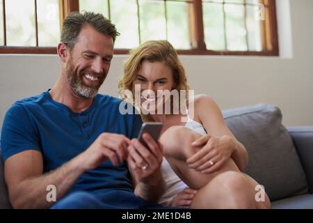 Le coppie felici condividono i momenti felici. una felice coppia di mezza età che utilizza un telefono cellulare insieme sul divano a casa. Foto Stock